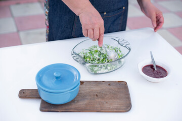 Close up of female wearing blue apron, standing, cooking, preparing food, mixing salad with spoon. Concept of cooking.
