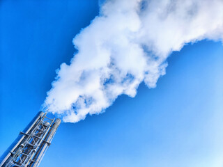 Air pollution by smoke coming out of factory chimney. White clouds of smoke against a blue sky background