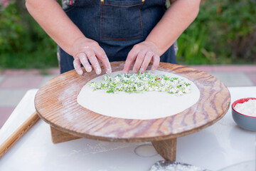 Close up of old female cook, chef wearing apron making pita, putting cheese filling on dough. Concept of fast food.