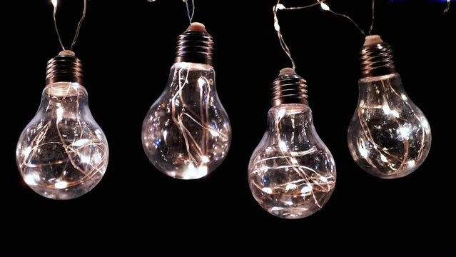 Lots Hanging Flickering Glowing Vintage Edison Light Bulbs on a Black Background. In a row. Christmas decorations, vintage electric light bulbs turn on and off, retro style garland illuminate space.