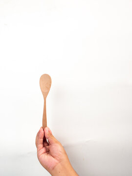 hand holding wooden tablespoon on gray background