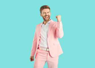 Portrait of a young overjoyed happy man with beard wearing stylish pink suit making yes winner's...