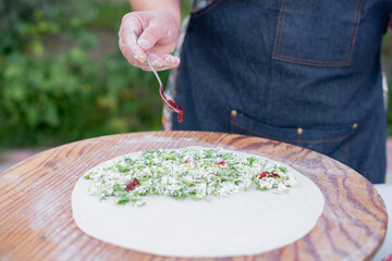 Close up of female cook, chef wearing apron rolling dough, putting filling, pouring sauce, making pita. Concept of fast food.