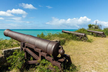 A row of three ancient cannons pointed toward the harbor at Fort James on the island of Antigua in...