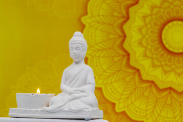 Close up of white marble figurine of Siddhartha Gautama, known as Buddha, with candle burning and...