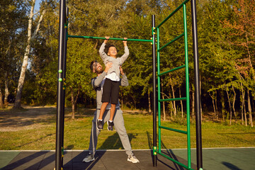 Young father or man coach teaching and helping a child boy to pull up himself on horizontal bar in...