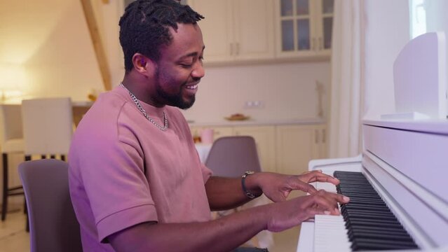 Talanted african american guy pianist playing piano and singing at home.