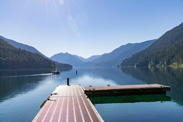 Panoramic view with sun ray lens flares over tranquil waters with mountains of Lake Crescent,...