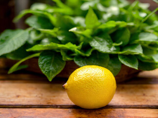 a ripe lemon sitting on top of a wooden table next to a leafy green leaf on top of a piece of wood