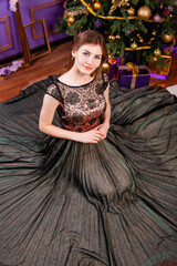 Fototapeta premium Top view, portrait of a young woman in an elegant dress sitting near a Christmas tree.