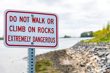 Close up of a white sign with red letters along a rocky coastline warning not to climb or walk on...