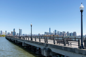 Fototapeta na wymiar Panoramic view from the over water foot and bike path in Liberty State Park, Jersey City, NJ, USA with one single person on a bicycle, with views of Manhattan and Jersey City skyscrapers