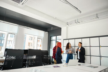 View to male and female colleagues talking in far corner of the office