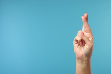 Woman crossing her fingers on light blue background, closeup. Space for text