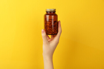 Woman holding jar with vitamin capsules on yellow background, closeup