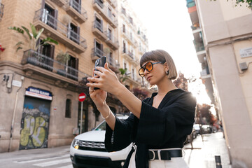 Adorable cute lady is making selfie in sunlight on city background 