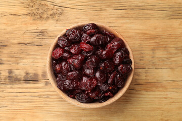 Tasty dried cranberries in bowl on wooden table, top view