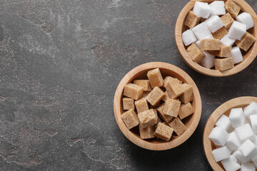 Different sugar cubes in bowls on gray textured table, flat lay. Space for text