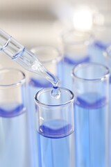 Laboratory analysis. Dripping light blue liquid from pipette into glass test tube on blurred background, closeup