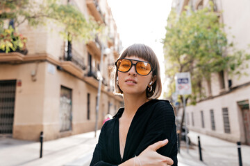 Stylish modern woman with short hair wearing modern glasses posing to camera in sunlight 