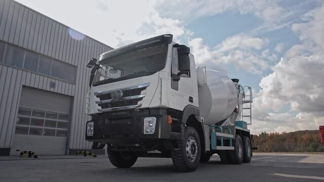 New clean concrete mixer truck moves against the backdrop of an industrial area. 