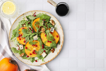 Tasty salad with persimmon, blue cheese, pomegranate and walnuts served on white tiled table, flat lay. Space for text