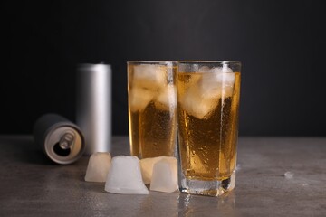 Tasty energy drink with ice cubes in glasses and aluminium cans on grey table