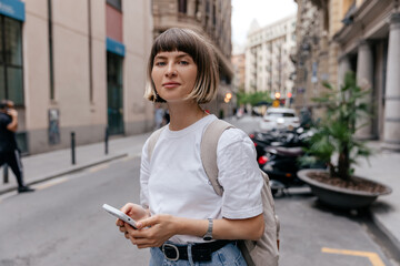 Naklejka na ściany i meble Woman with stylish short hair texting on smartphone outside
