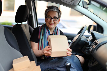 Happy woman driver sits inside a car with boxes in hands, smiling, portraying a modern and cheerful...