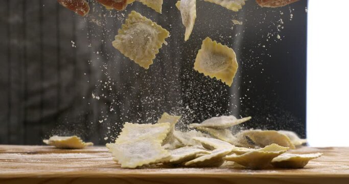 Super slow motion close up of professional artisan baker chef is mixing with flour homemade traditional recipe fresh pasta ravioli on rustic wooden table in traditional bakery kitchen.
