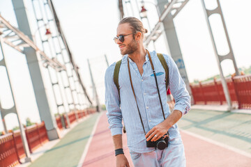 Young attractive man with photocamera exploring a new city with a backpack behind by walking...