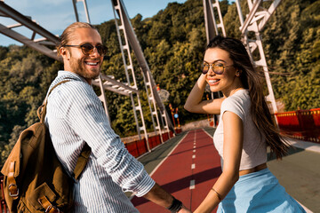Beautiful young couple enjoying moments together looking at camera and smiling while walking outdoors on a romantic date, trip, travel voyage sightseeing