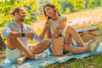 Young man offers a bit of chips to his girlfriend and they drinking beer. Couple enjoying their...