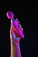 The girl is holding a sex shop toy. Sex toy clitoral vibrator on a black background with neon...