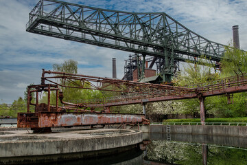 Fototapeta na wymiar Low angle view of an abandoned and dilapidated water purification basin of an industrial steel mill in public Landschaftspark, Duisburg, Germany with cranes and building in background