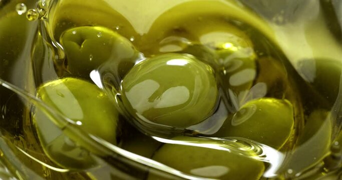 Super slow motion macro of fresh ripe olive is falling in bio organic golden liquid extra virgin olive oil with splashing drops on ripe olives at 1000 fps.