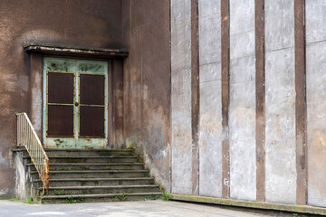 Fototapeta na wymiar Close up of stairs with rusty entrance door of building of an abandoned and dilapidated industrial steel mill in public Landschaftspark, Duisburg, Germany with striped pattern concrete on facade