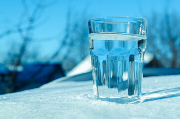 A glass of clean water stands on clean white snow