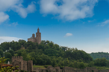 Panorama of the old Bulgarian medieval fortress under blue sky. A stone bridge leads to an ancient castle on a green hill. A beautiful view of the historical place. Concept of tourism and travel.