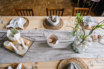 Setting table for Easter dinner with candles, ceramic plates with easter eggs in nest, Easter bunny made of linen napkin. Holidays celebration concept. From above place. Top view. Easter decor. Set up