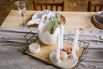 Easter decor with candles, easter quail eggs in nest, vase with flowers at home. Setting table for...
