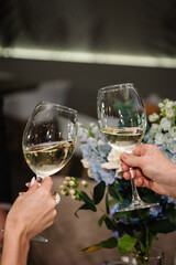 Cheers. Romantic date by candlelight at night. Couple in love drinking white wine. Hands man and woman hold glasses at home. Toast. Dinner setup table for couple on Valentine's day. Closeup.