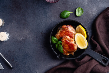 Roasted chicken thighs in cast iron slillet with lemon slice, high angle view, dark gray background