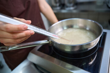 Experienced female cook checking temperature of syrup during cooking