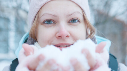 Sweet beautiful happy smiling winter girl blowing snow. Close up.