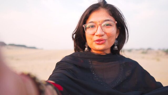 Selfie video of Young Indian woman  at desert in Jaisalmer, Rajasthan, India. Happy smiling girl vlogging in camera. Attractive girl traveler use mobile phone record video vlogging. 