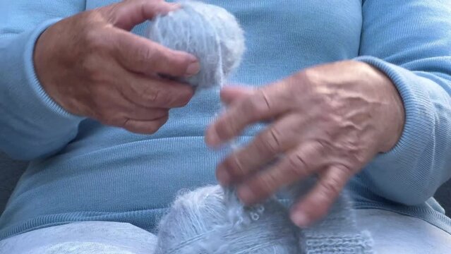 Hands of an old woman with a ball of woolen thread. Woman with knitting in her hands. A fascinating close-up of the handicraft process. Knitting concept, retired tranquil carefree life .
