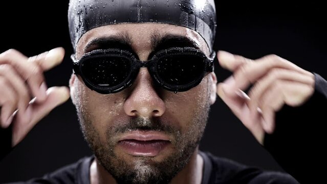 Swimmer, face and goggles on man for fitness with water sport, workout and determination on black background. Challenge, competition and confident with training, exercise and portrait for swimming