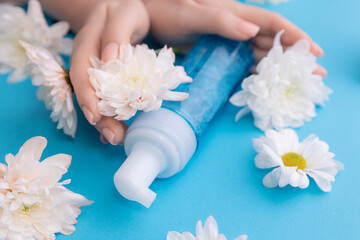 Obraz na płótnie Canvas Concept natural cosmetics for facial skin care. Woman hands with bottle with water foam for cleansing on blue background with white flowers, top view