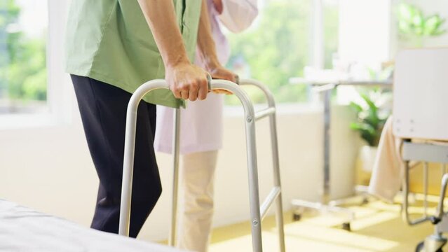 Close up hands of young patient man walk using walker to practice in room of hospital and support by doctor stand beside the patient.